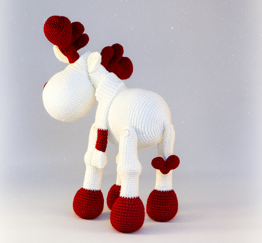Knitted reindeer toy with red antlers andhooves on a light gray background