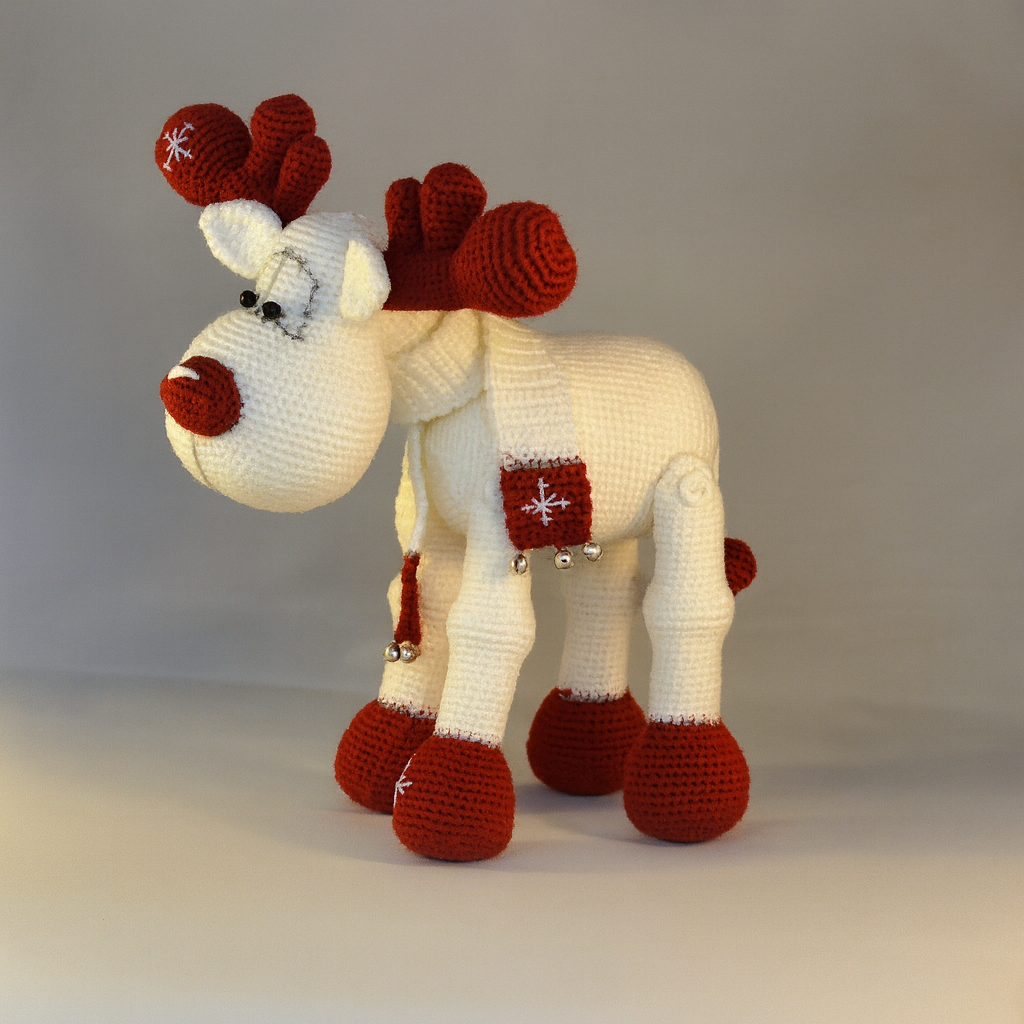Knitted reindeer toy with red antlers and hooves on a plain background