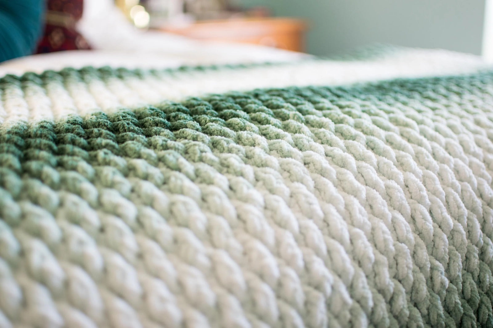 Close-up of a textured green and white crochet blanket on a bed.