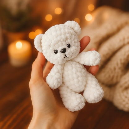 White crochet teddy bear held in a hand with a warm, blurred background