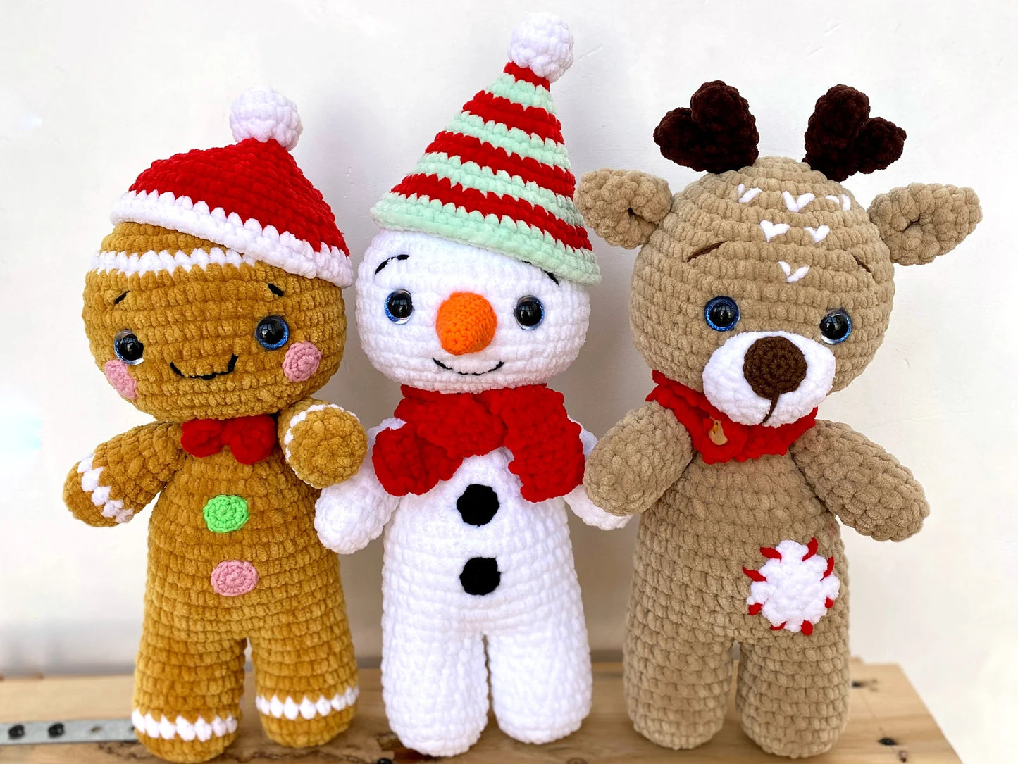 Three crocheted Christmas-themed dolls: a gingerbread man, snowman, and reindeer, on a light background.