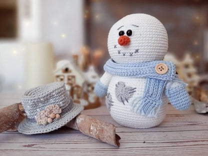 Crocheted snowman toy with a blue scarf and hat on a wooden surface.