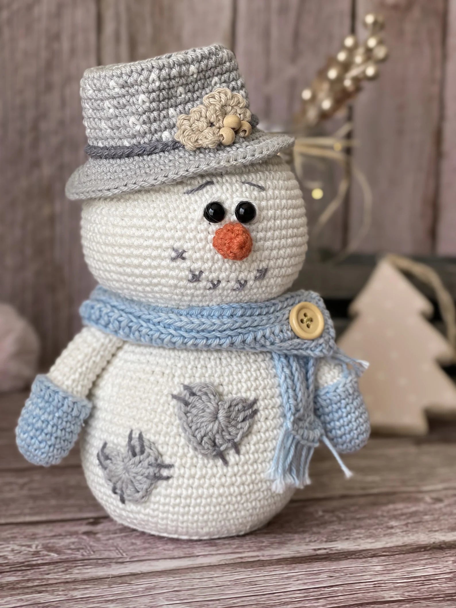 Crocheted snowman toy with a top hat, scarf, and gloves on a wooden surface.