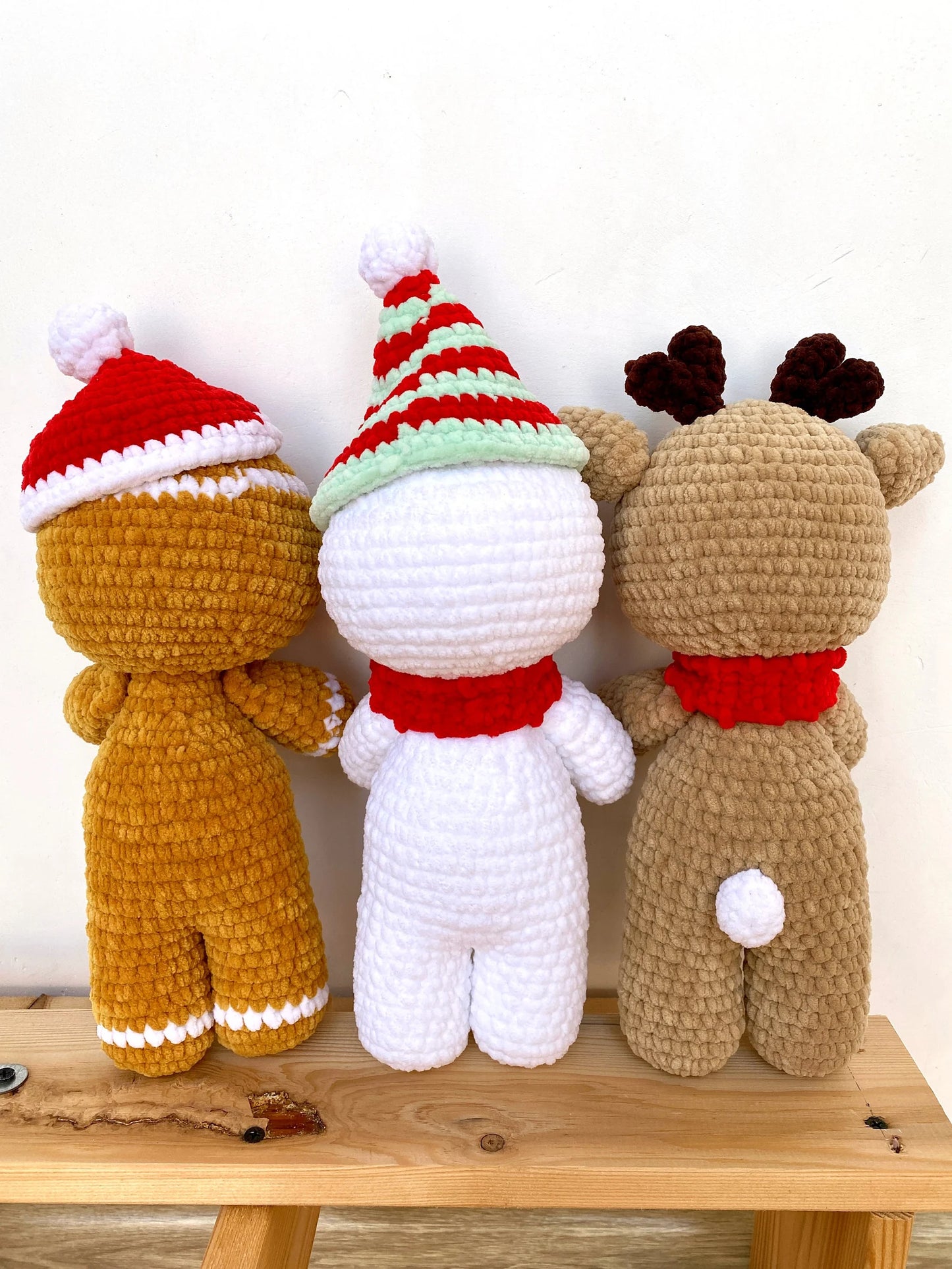 Three crochet toys dressed in Christmas-themed outfits on a wooden surface.