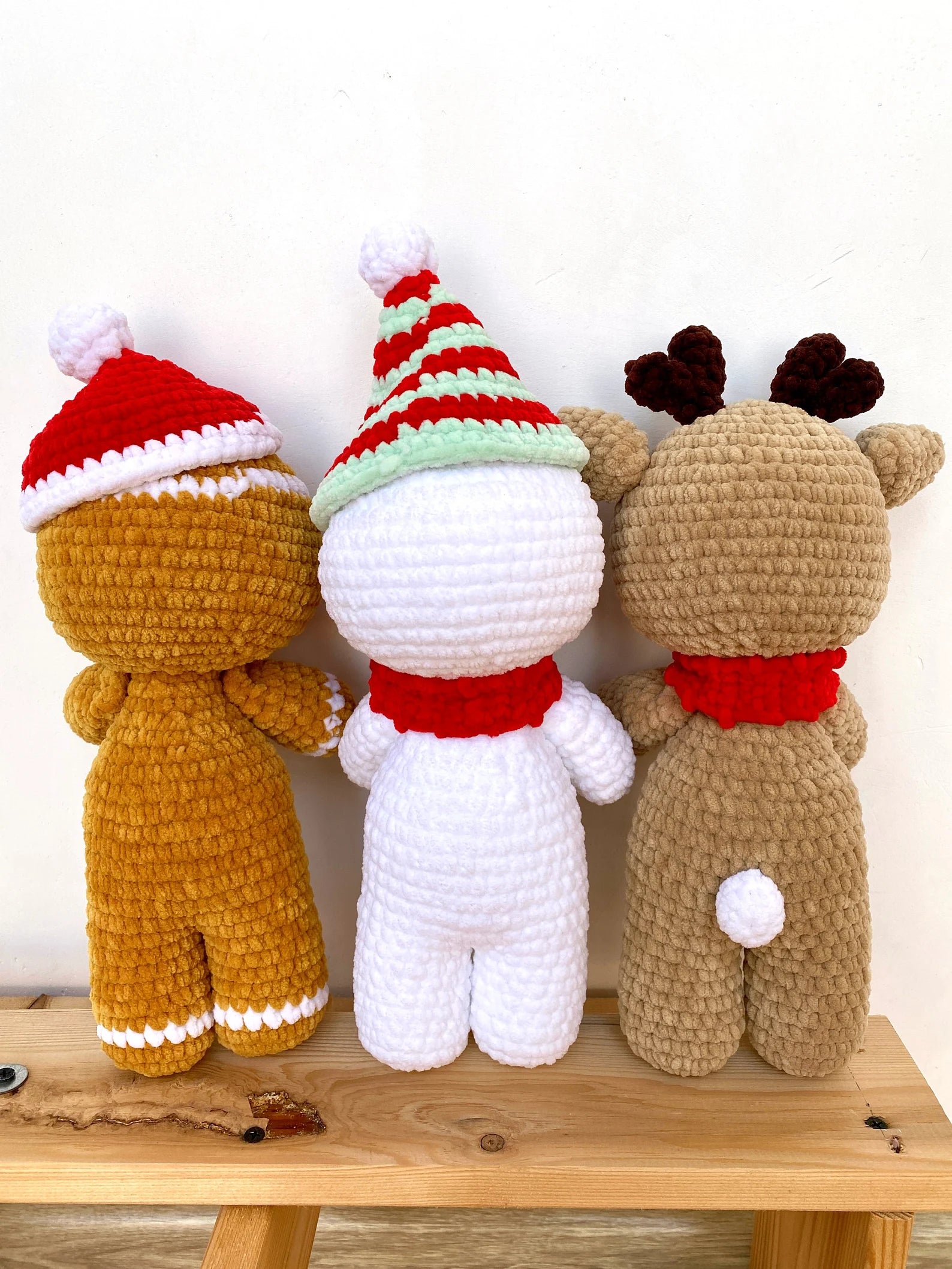 Three crochet toys dressed in Christmas-themed outfits on a wooden surface.