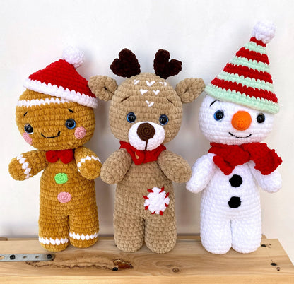 Three crocheted Christmas-themed toys including a gingerbread man, reindeer, and snowman on a wooden surface.