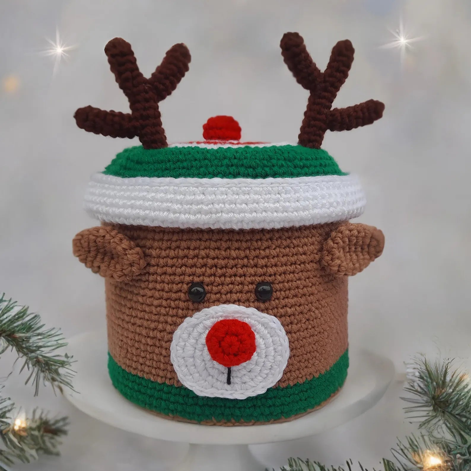 Crocheted reindeer hat with antlers and a red nose on a white background