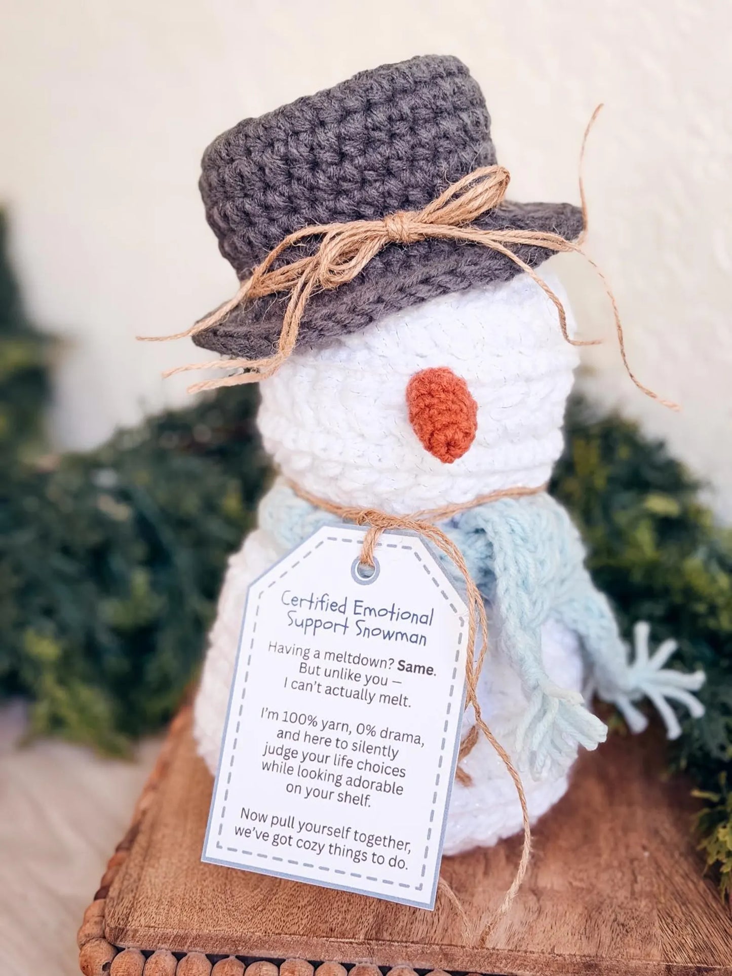 Handmade snowman figurine with a tag, surrounded by greenery