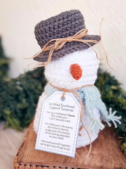 Handmade snowman figurine with a tag, surrounded by greenery