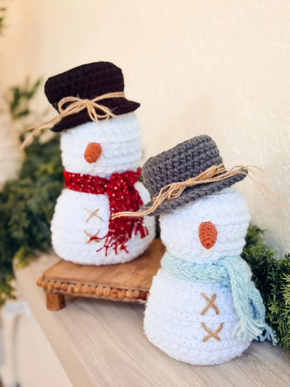 Two crocheted snowmen with scarves and hats on a wooden surface with a blurred background.