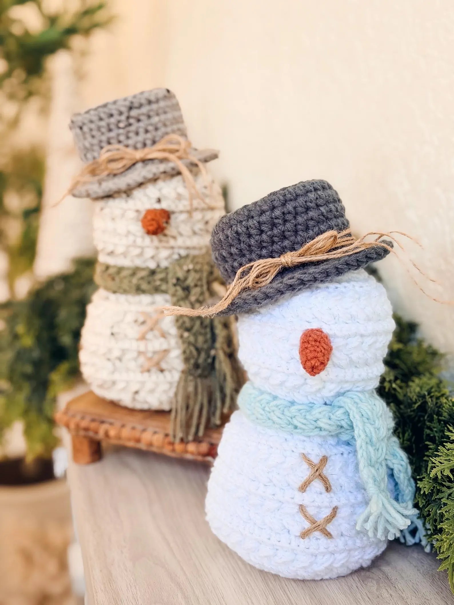 Two crocheted snowmen with hats and scarves on a wooden surface.