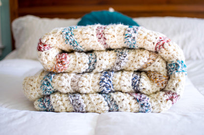 Stack of colorful knitted blankets on a bed
