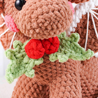 Close-up of a crocheted reindeer with red nose and holly leaves on a white background
