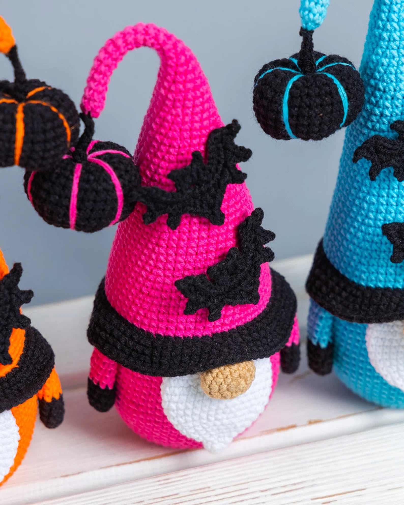 Crocheted Halloween-themed gnomes with pumpkins and bats on a light background